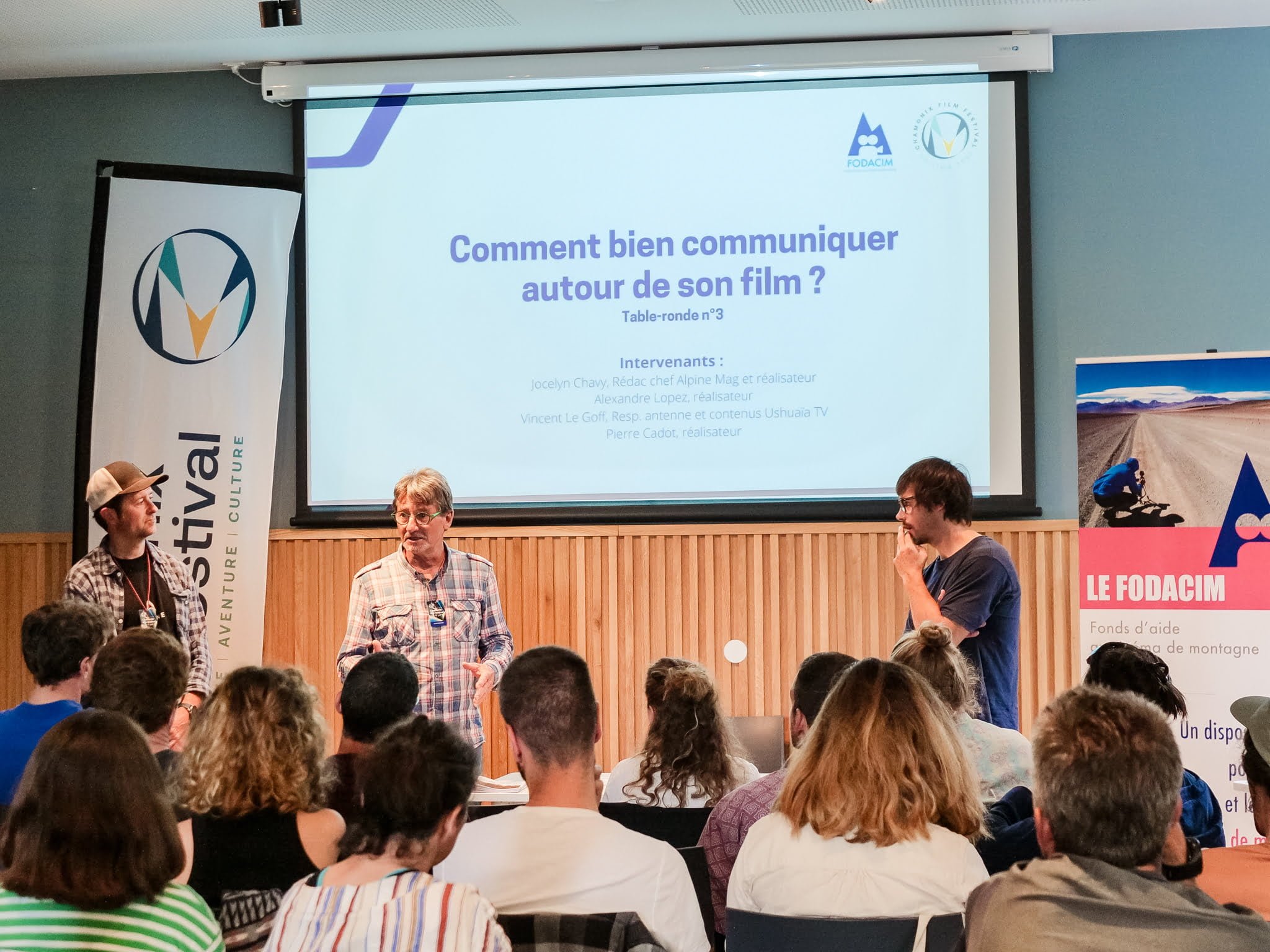©CFF2023-008 Trois personnes parlent devant une assemblée d'une dizaine de personnes. Un écran sur le mur indique la troisième conférence de la journée qui s'intitule Comment bien communiquer sur son film ?